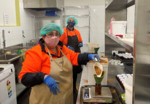 2 employees in the food processing room pouring spices into jars